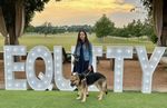 Haben and her guide dog Mylo standing in front of giant light-up letters spelling "Equity" with beautiful green fields in the background.