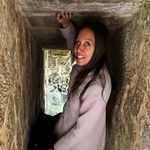 I'm wearing a gray coat and smiling as I stand at the curved stone entrance to a short tunnel.