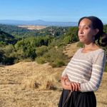 I'm standing on a ridge overlooking the green and yellow hills of Portola Valley. My arms are crossed, and Mylo's leash is looped through an arm.