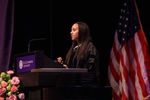 Haben is standing at the St. Catherine University podium wearing academic regalia, and behind her is a US flag.