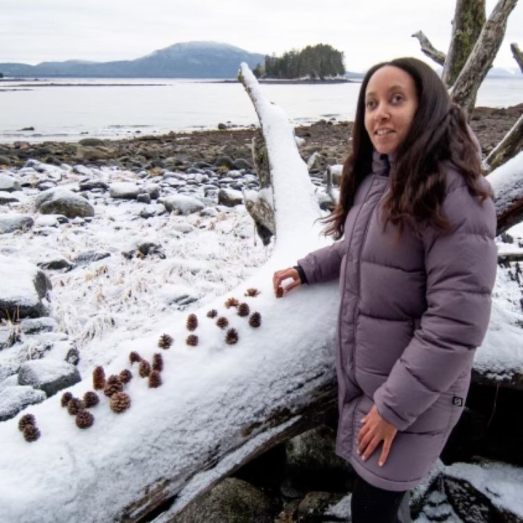 Brailling on a beach in Alaska. A small, secluded island full of evergreens sits in the middle of Gastineau Channel, and on the far shore rise mountains. I’m smiling as I hold a cone on top of a large, snow-covered log. The log has twenty-five Spruce and Hemlock cones half submerged in snow. The cones spell: brrraille! Photography by Cameron Byrnes.