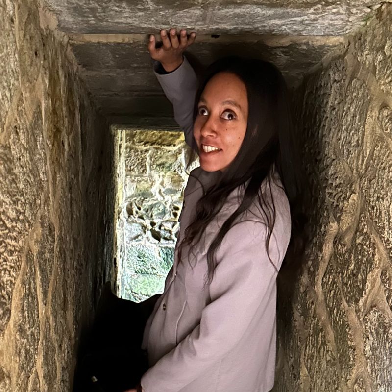 I’m wearing a gray coat and smiling as I stand at the curved stone entrance to a short tunnel.