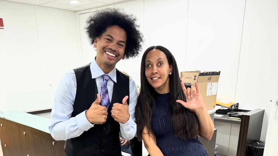 Haben and Mychal Threets standing together and smiling. Mychal is doing two thumbs up, and Haben is making the ILY sign.
