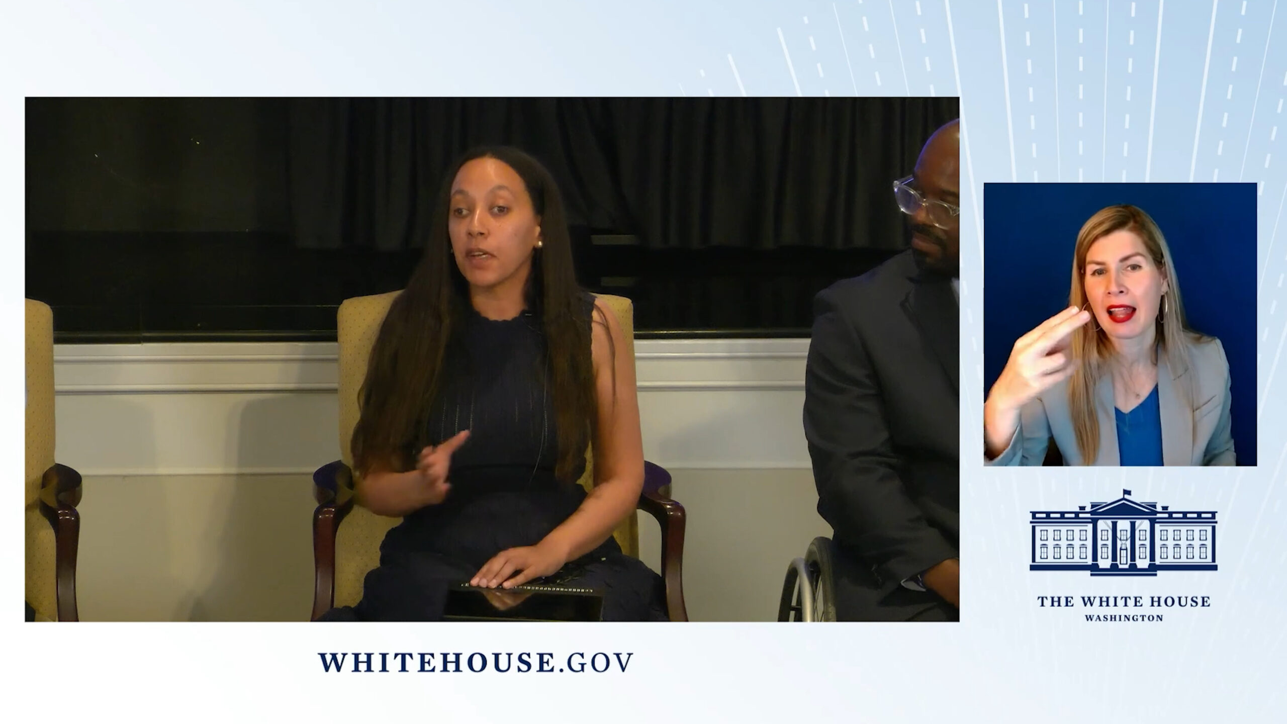 Haben sitting on a stage speaking. An ASL interpreter is shown on the right